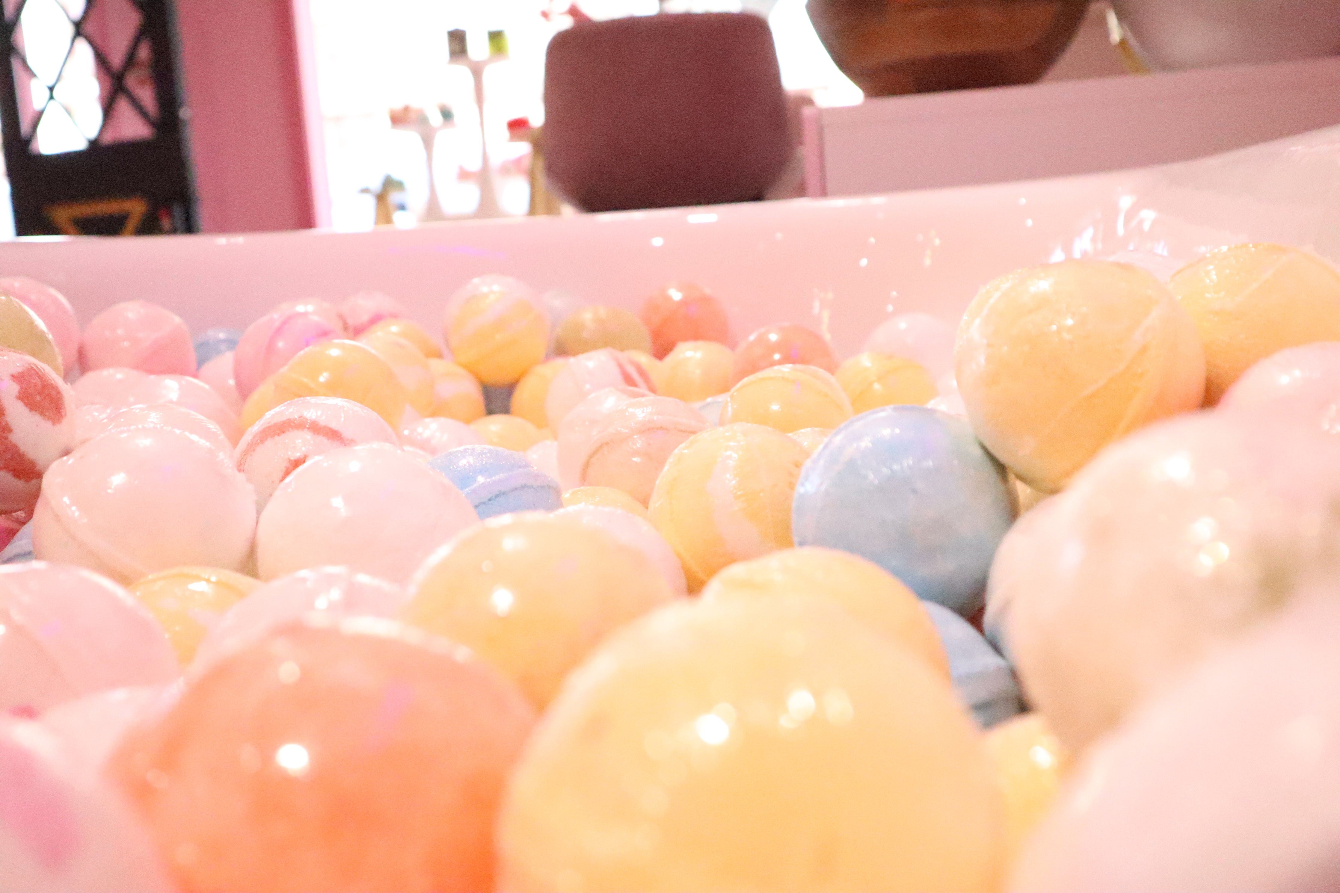an upclose shot of a light pink bath tub filled with pastel colored Skinderella bath bombs.